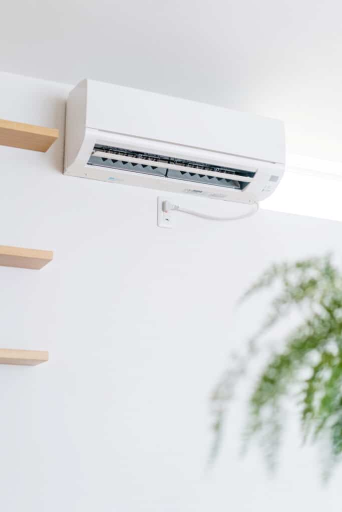 Climatiseur Mural Blanc: Installation Facile & Efficace Climatiseur mural blanc branché sur une prise électrique 200V, près d'étagères en bois, dans un intérieur lumineux.