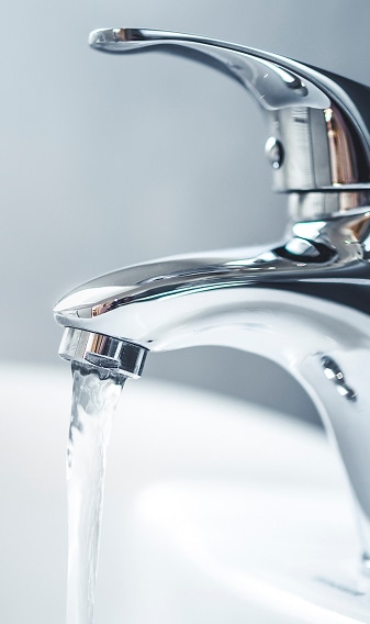 Robinet de salle de bain chromé, eau claire, gros plan Gros plan d'un robinet de salle de bain chromé moderne avec un jet d'eau clair coulant dans un lavabo blanc.
