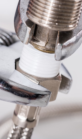 Serrage raccord plomberie clé à molette connexion Closer sur une clé à molette serrant un raccord de plomberie, avec filetage et ruban PTFE blanc visible.