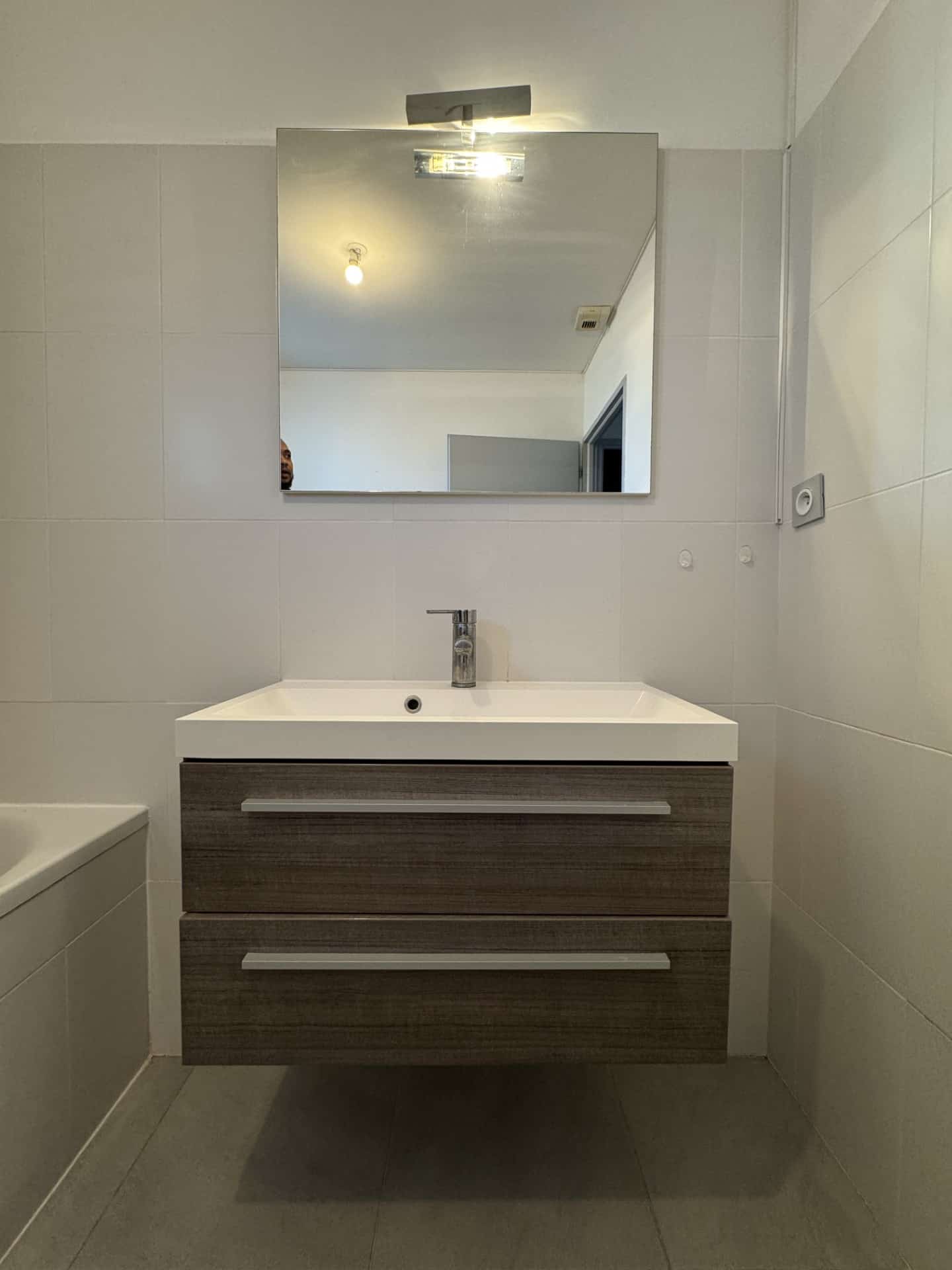 Meuble vasque suspendu en bois, lavabo blanc et grand miroir dans une salle de bain carrelée.