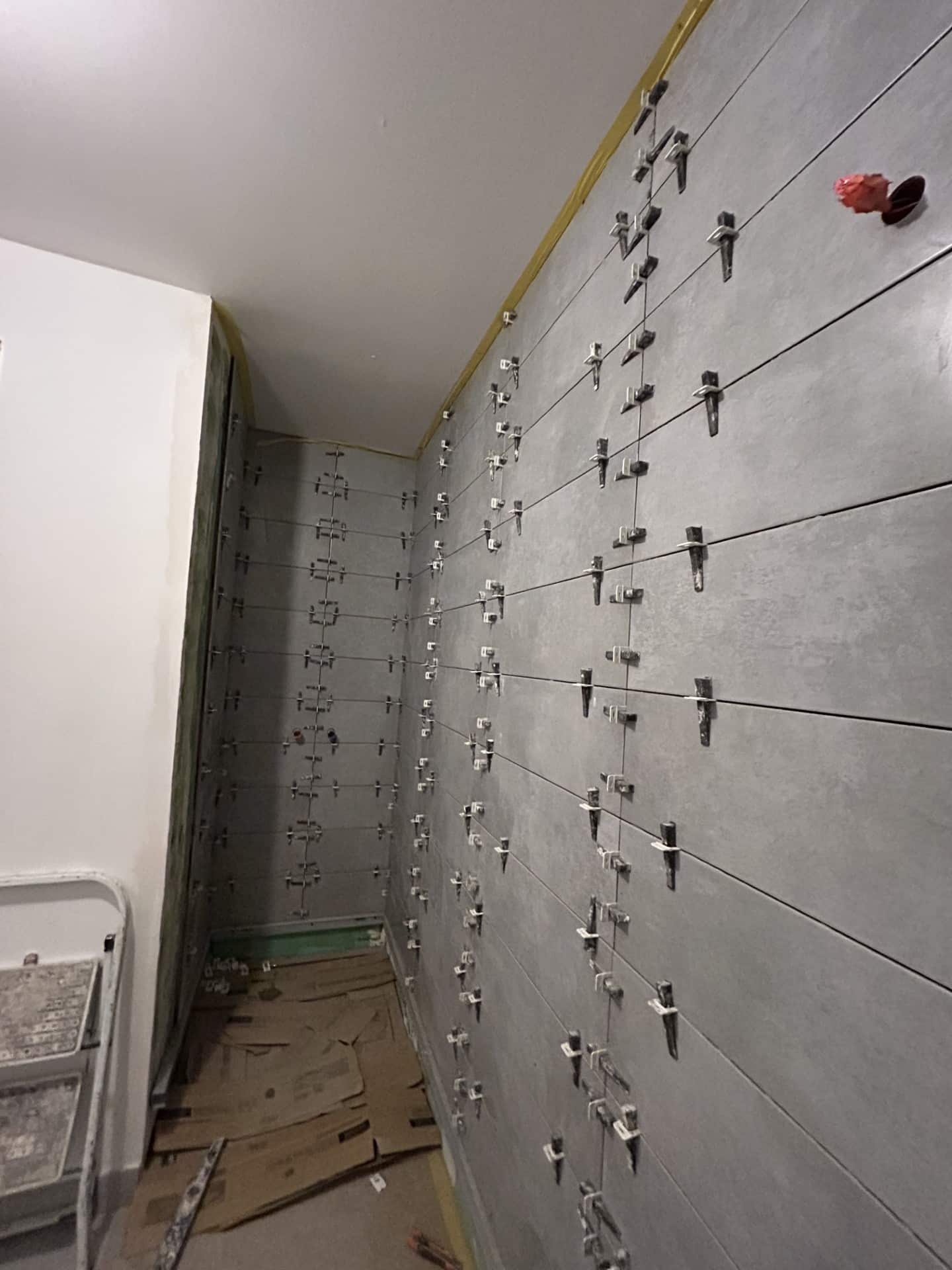 Pose de carrelage gris avec croisillons de nivellement sur un mur en rénovation.