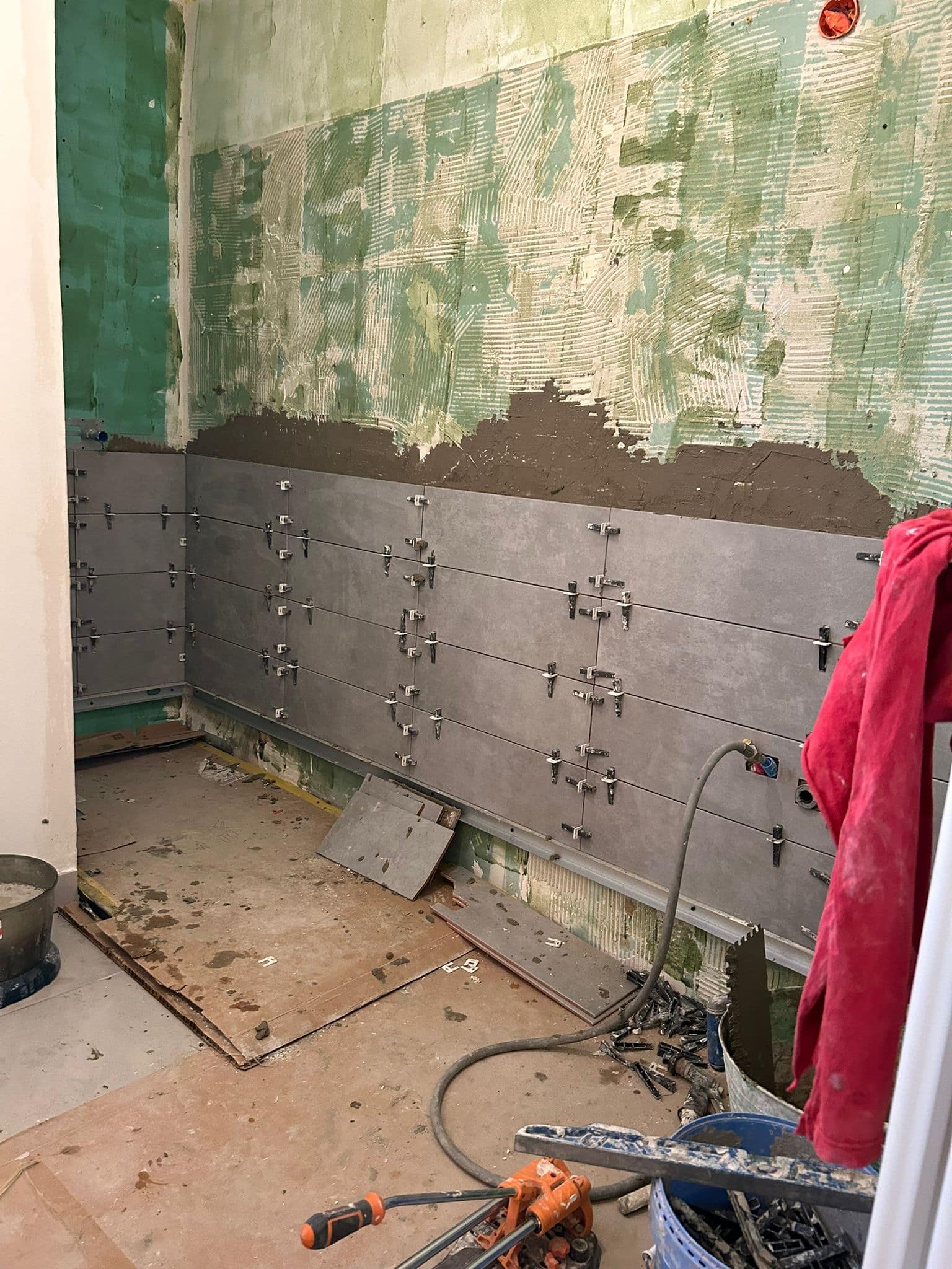 Pose de carrelage gris mural avec croisillons dans une salle de bain en chantier.