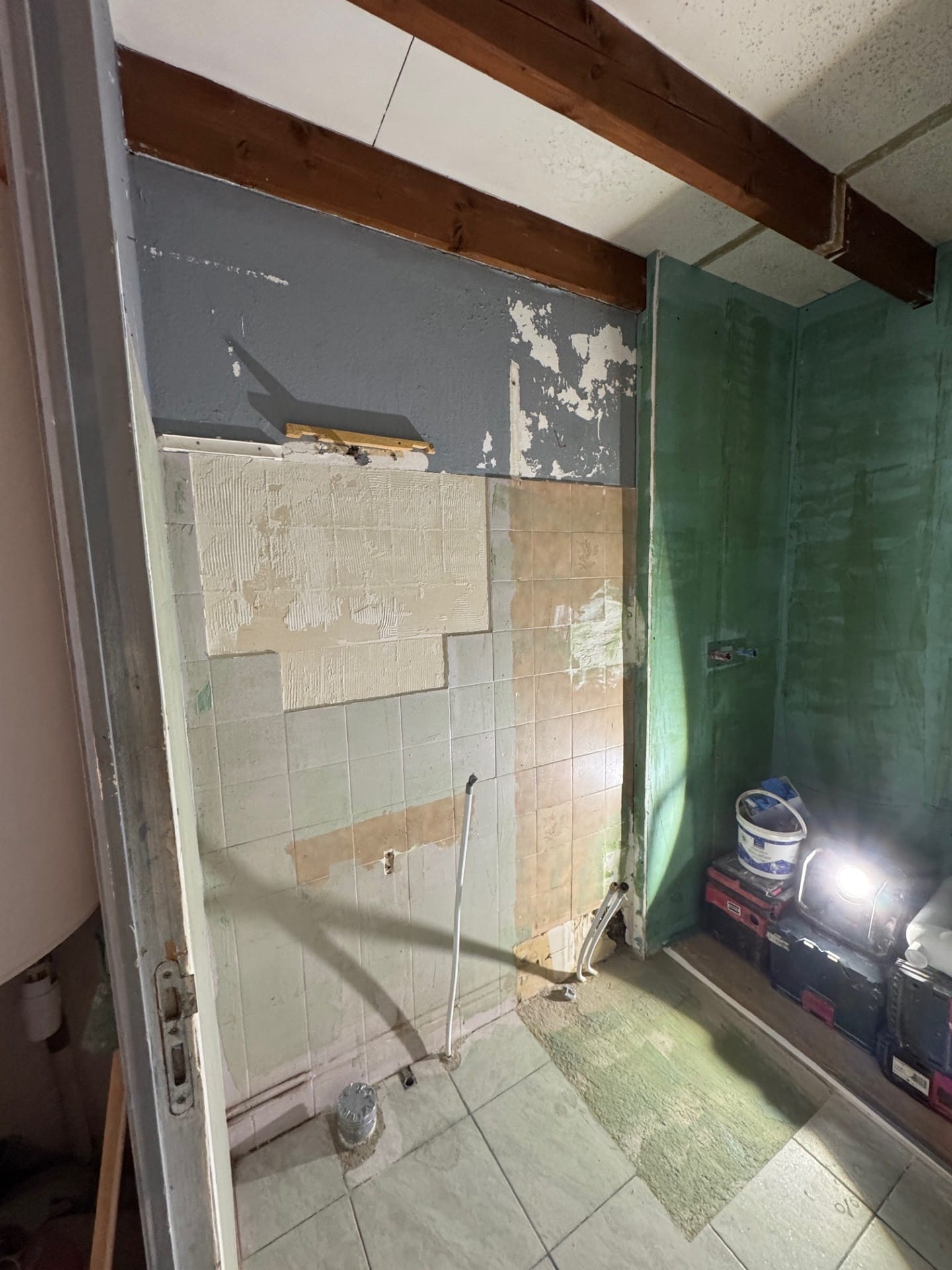 Rénovation salle de bain : murs dénudés, étanchéité verte et poutres bois visibles.
