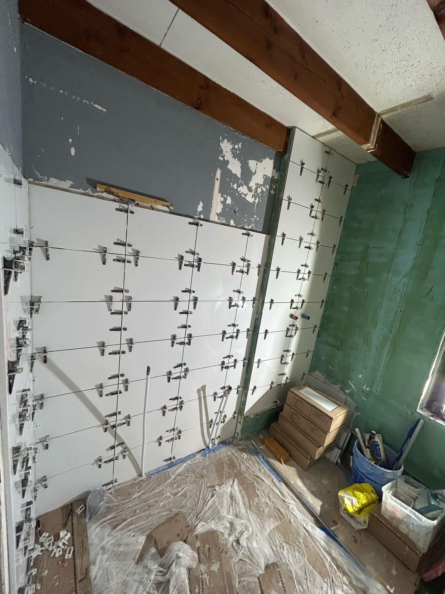 Pose de grands carreaux blancs avec croisillons nivelants dans une salle de bain en travaux.