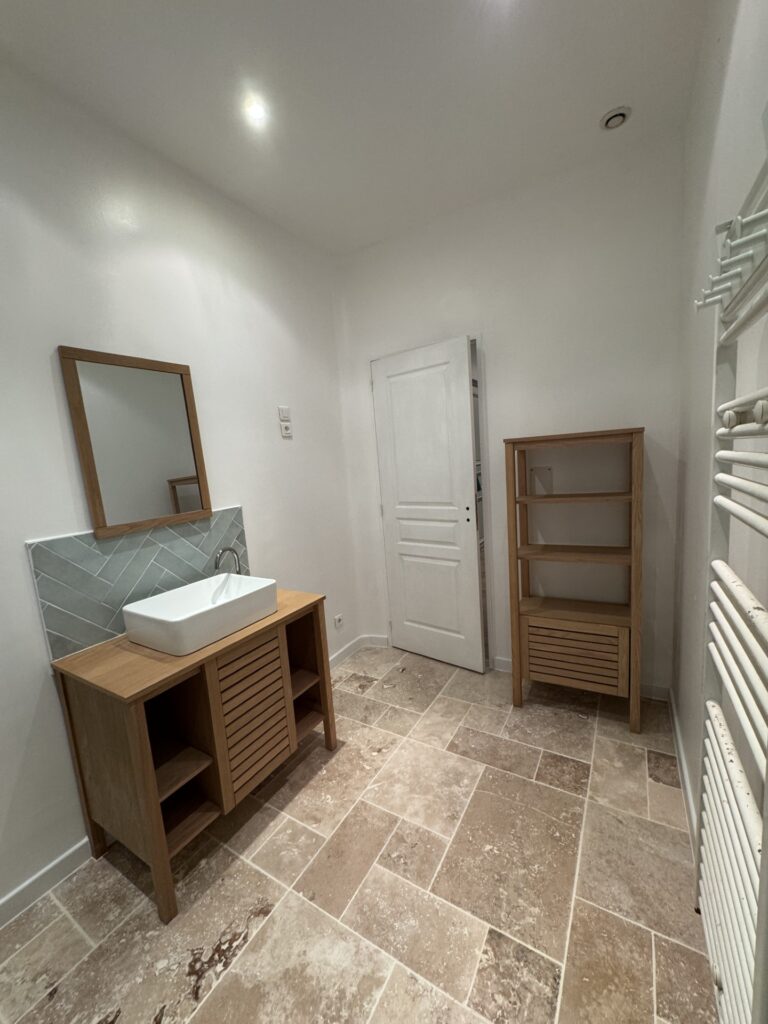 Meuble de salle de bain en bois et vasque moderne Salle de bain moderne avec vasque blanche, meuble en bois clair, dosseret gris et carrelage en pierre naturelle.