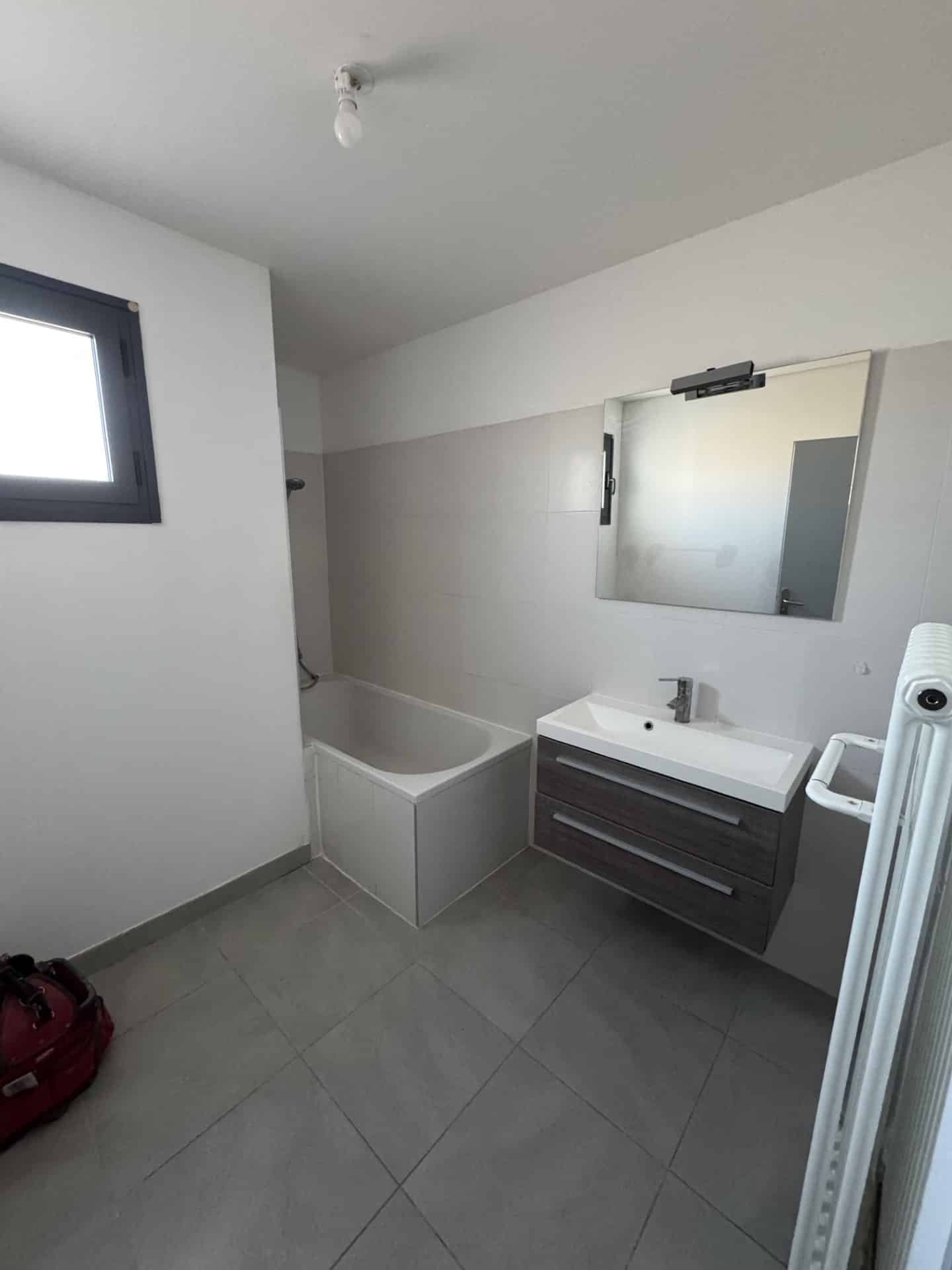 Salle de bain moderne avec baignoire blanche, meuble vasque suspendu bois et carrelage gris.