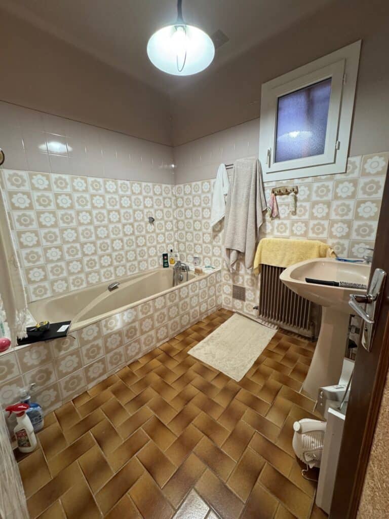 Salle de bain vintage avec carrelage fleuri beige Salle de bain vintage avec carrelage à fleurs beige, baignoire assortie et sol en terre cuite.