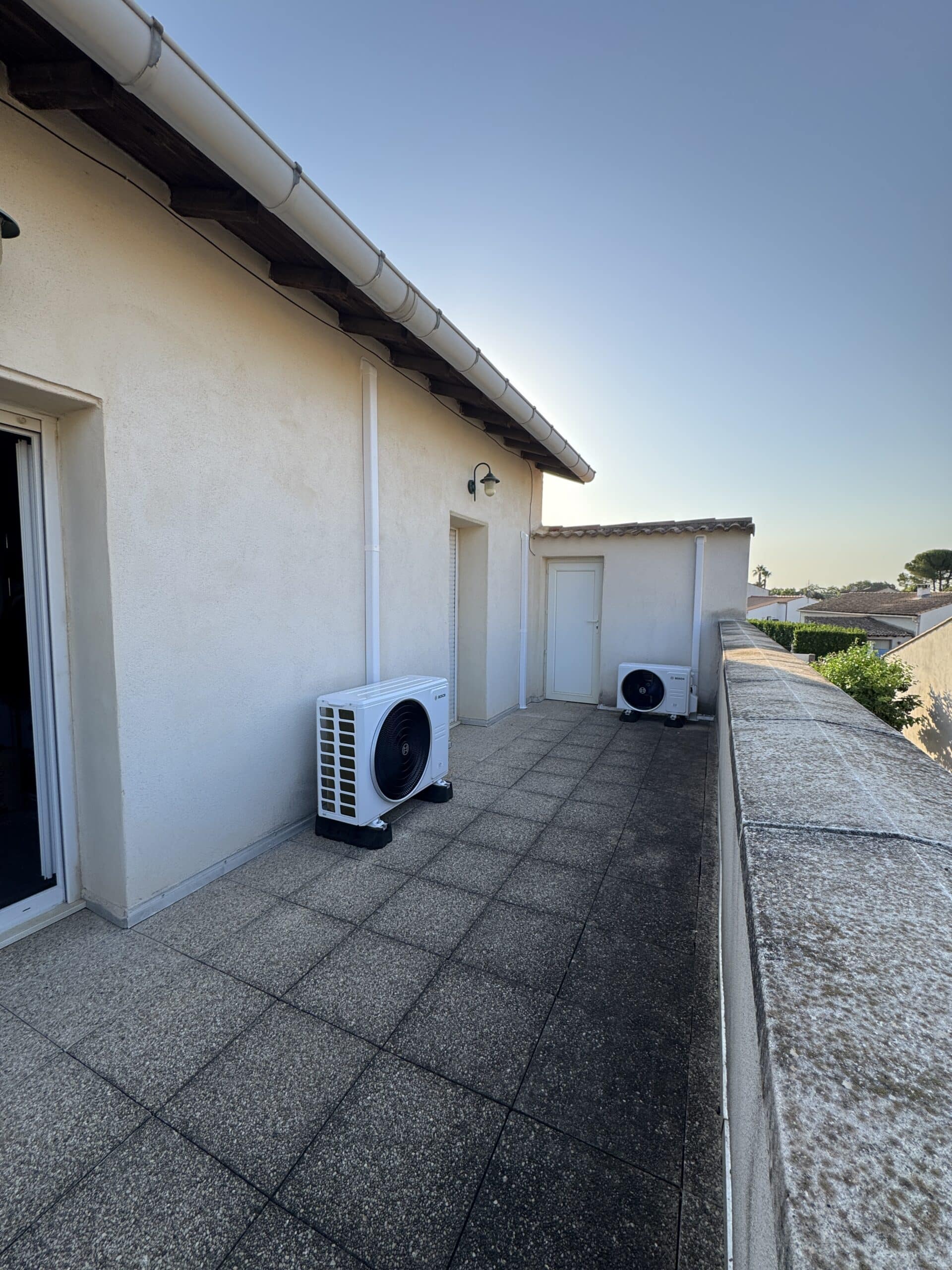 Deux unités de climatisation Bosch blanches sur un balcon carrelé avec mur en crépi clair.