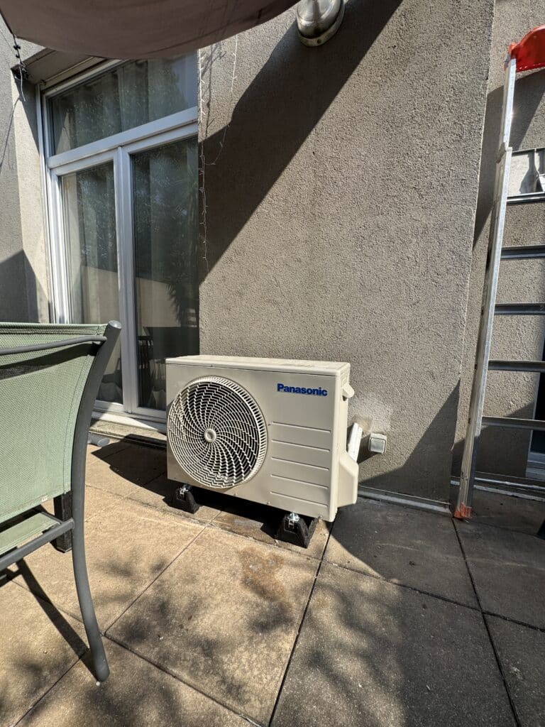 Installation de climatisation Panasonic sur terrasse Unité Panasonic sur terrasse, entre une porte vitrée et un mur gris.